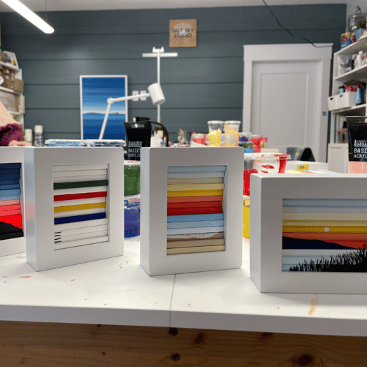 photo of four miniature wooden slat artworks in bright colours showing beach landscapes