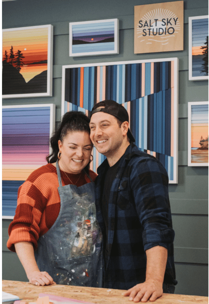 Photo of owners Kate and BJ smiling with their artwork in the background