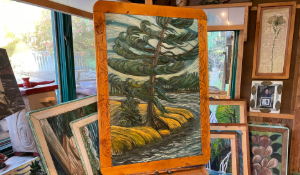 picture of a carving of a pine tree along a riverbank. The river is blue. Tree is green and blue on green grass.