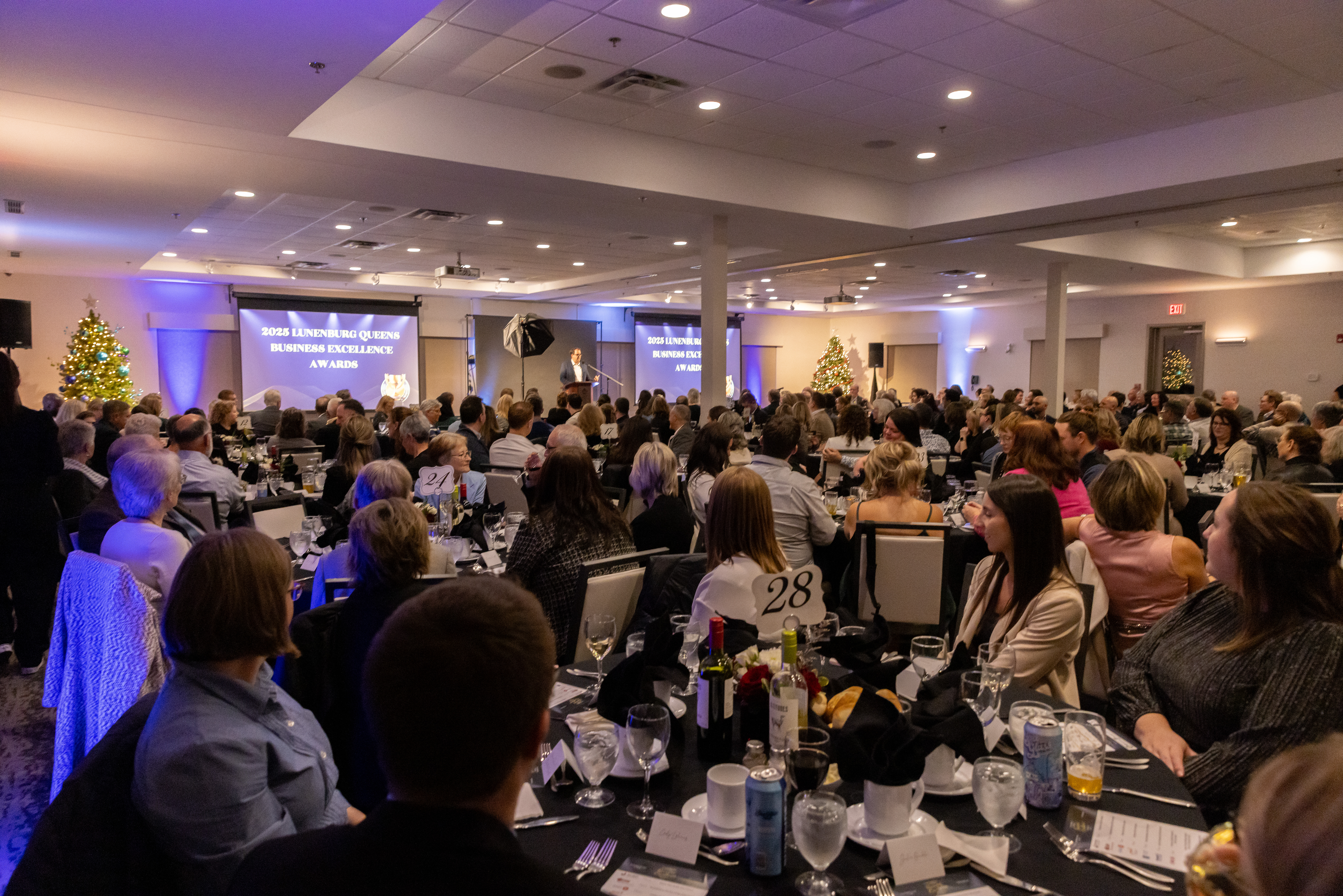 Photo of a large crowd seated around round dinner tables with centerpieces in a conference room